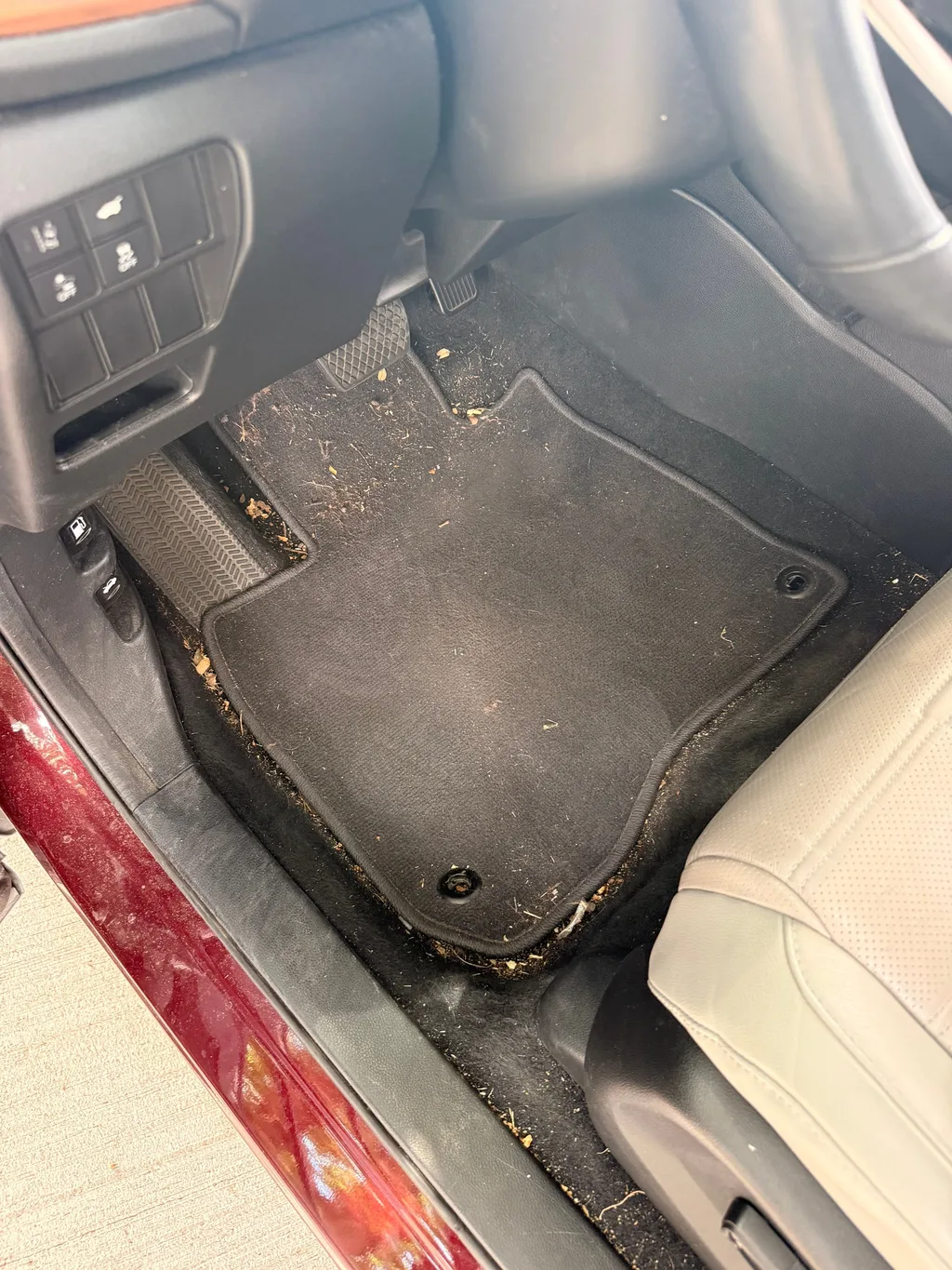 Driver floor mat of a red Honda CR-V before detailing, covered in grit, dried leaves and debris around the pedals